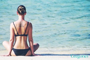 woman sitting by ocean doing yoga.